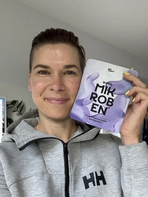 Person holding a purple packet labeled 'MIKROBEN' and smiling.