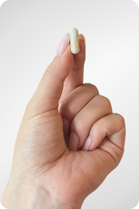 Hand holding a small capsule against a light background.