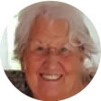 A smiling elderly person with white hair in a circular frame.