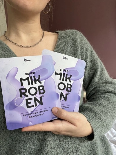 Person holding two packets labeled 'Super Mikroben' with purple design.
