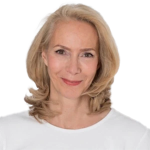 Smiling person with blonde hair wearing a white shirt against a plain background.