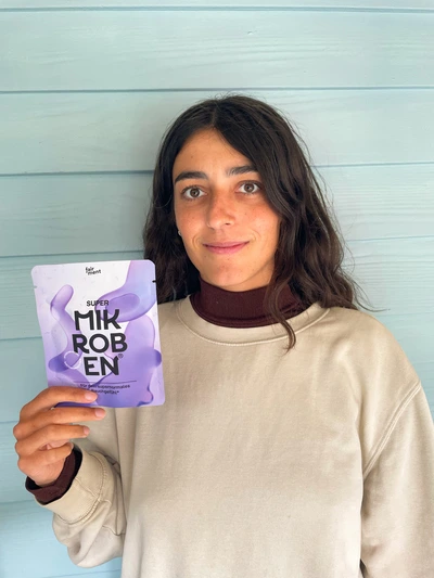 Person holding a purple product package against a light blue wall.