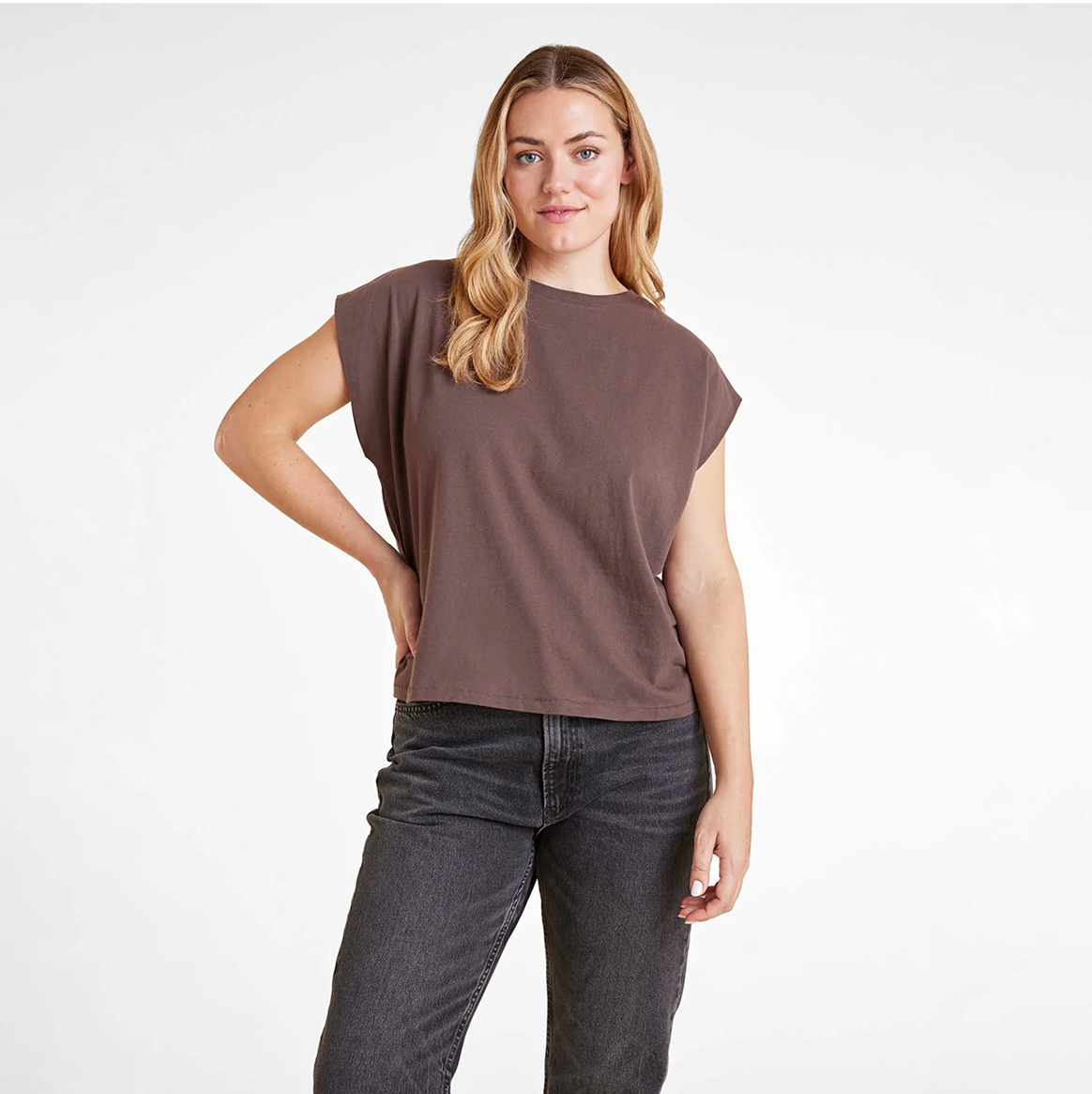 Person wearing a brown shirt and black jeans against a plain background.