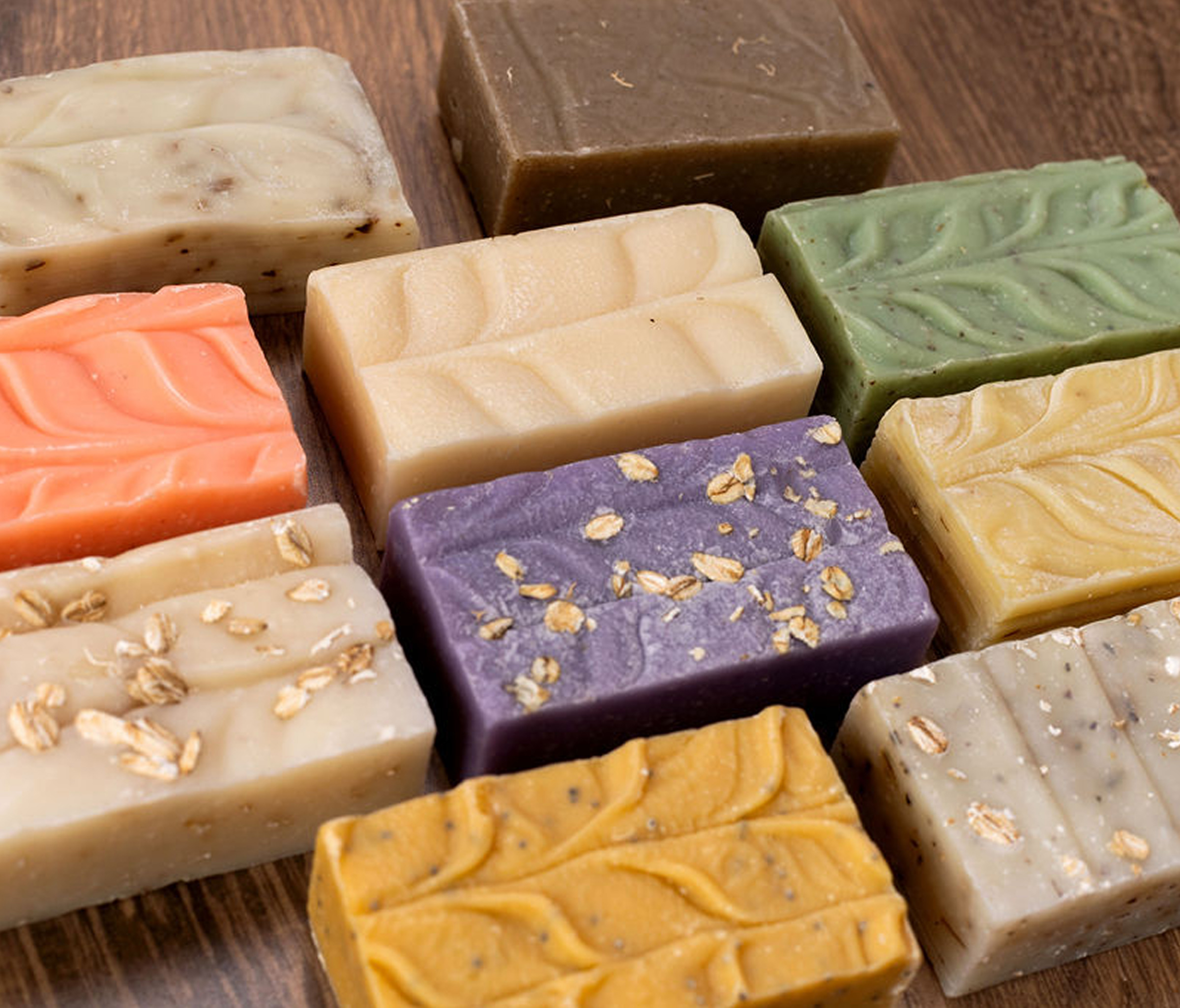 Assorted handmade soap bars with various colors and textures on a wooden surface.
