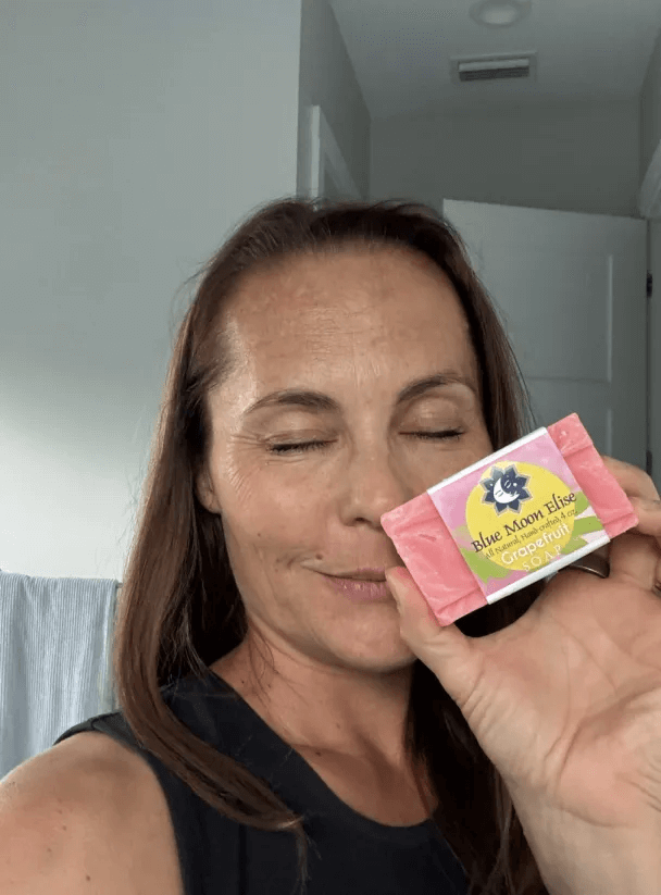 Person holding a bar of soap labeled 'Blue Moon Elise' with eyes closed.