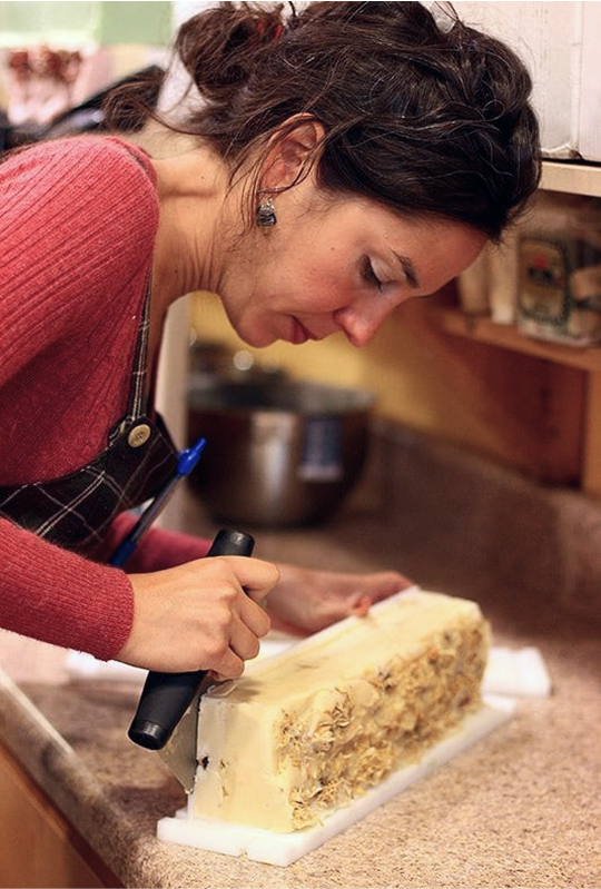 Person carving a large block of cheese on a kitchen counter.