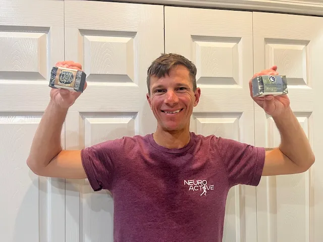 Person holding two bars of soap, smiling in front of white doors.