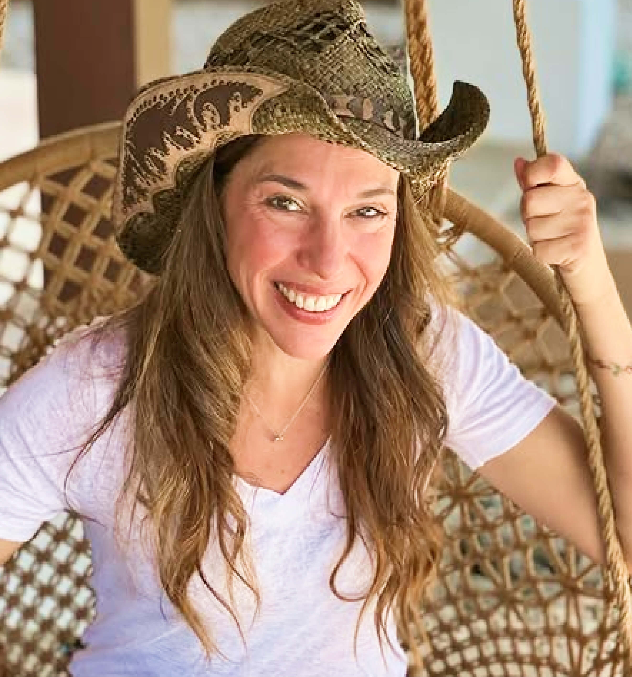 Smiling person wearing a cowboy hat, sitting on a woven swing.