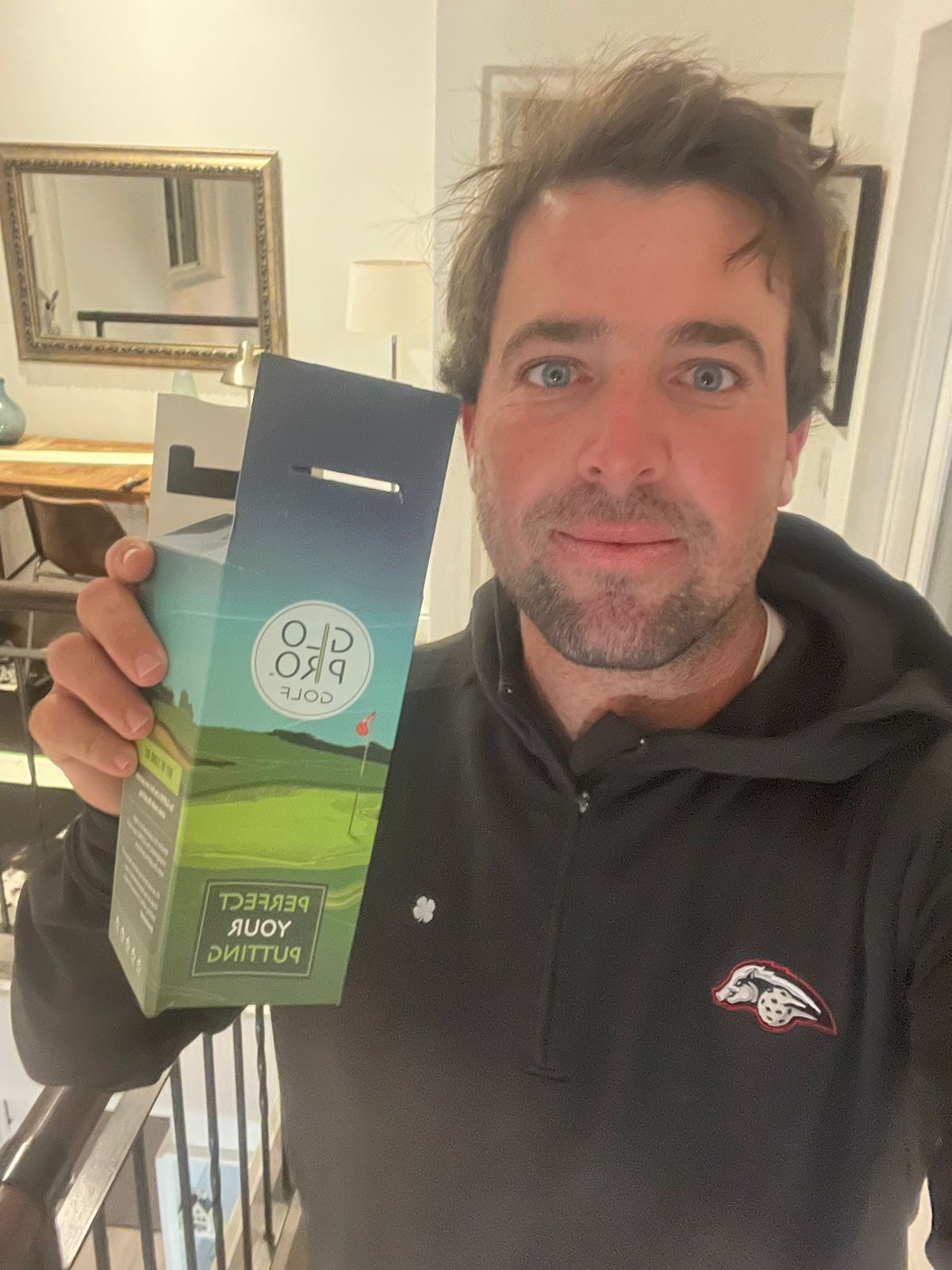 Person holding a golf product box with interior decor in the background.