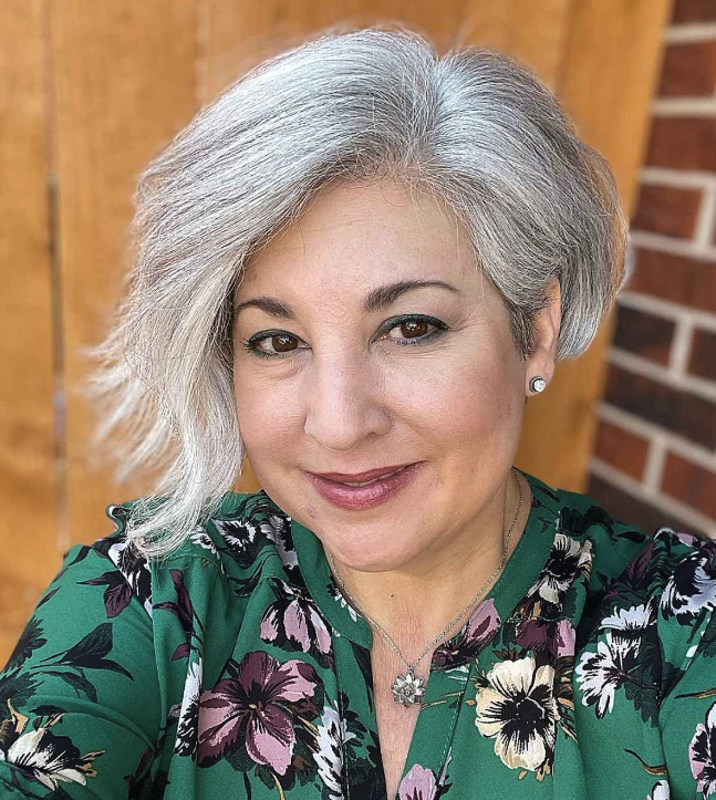 Person with short gray hair wearing a floral green top, smiling outdoors.
