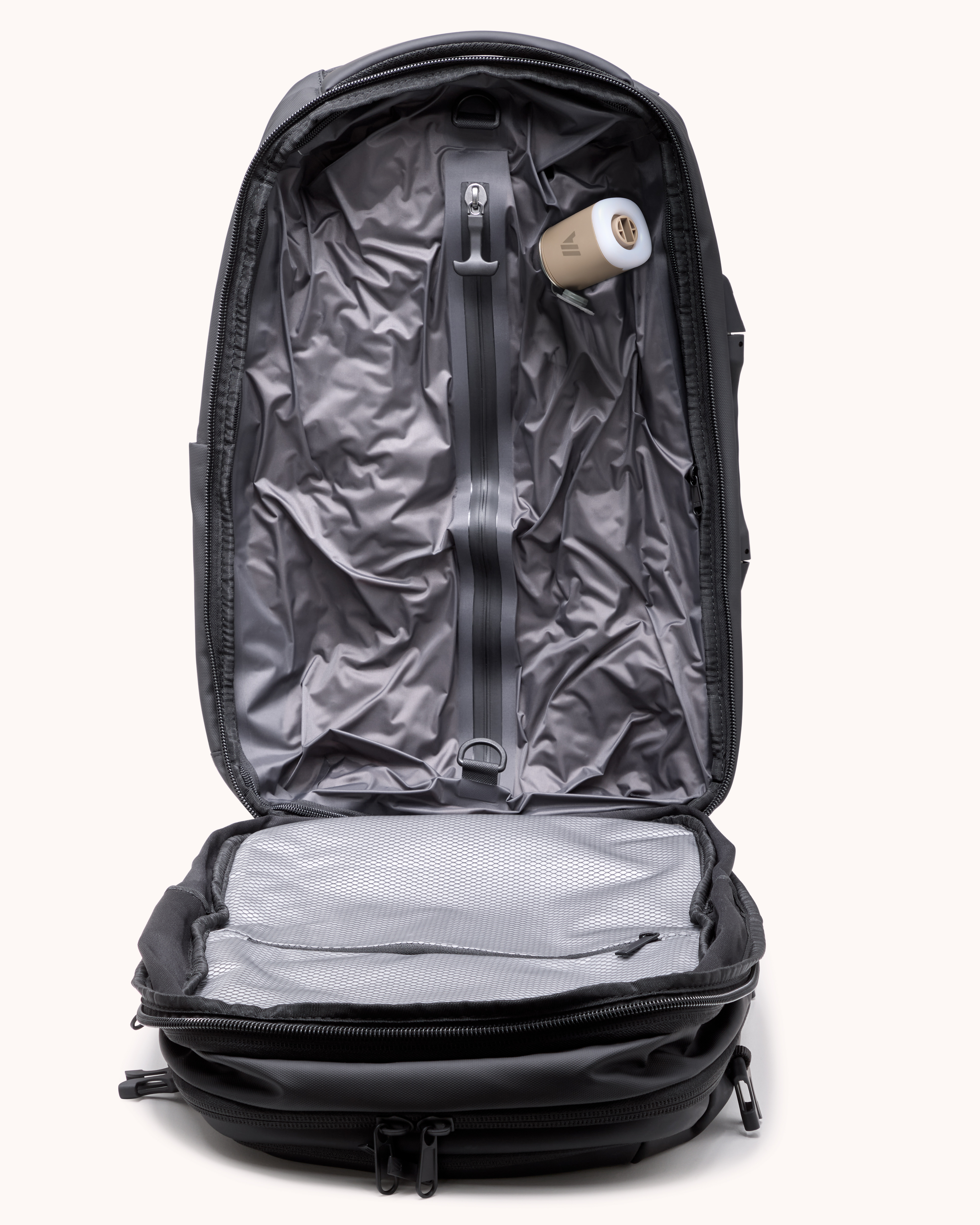 An open black backpack with a gray interior and a small beige electronic device inside.