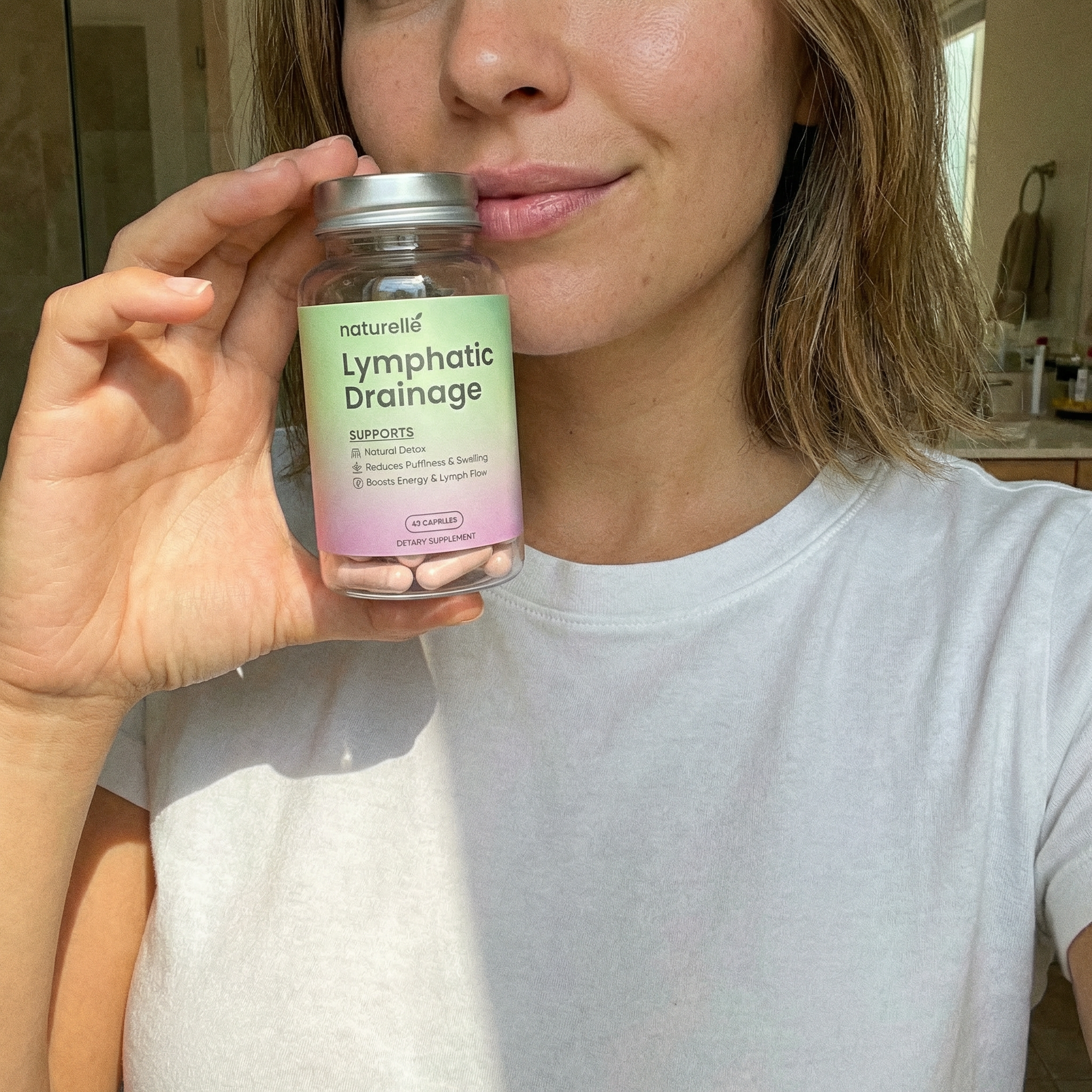 A woman in a white t-shirt holding a bottle of Naturellé Lymphatic Drainage dietary supplements.