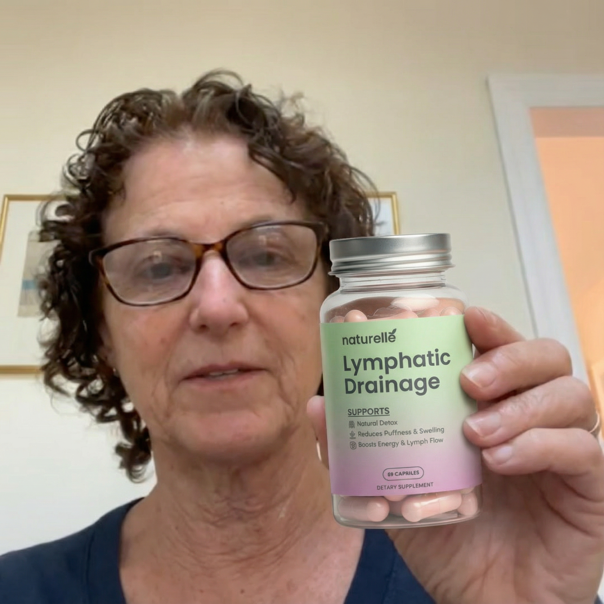 A woman with glasses holds up a clear bottle of Naturellé Lymphatic Drainage capsules.