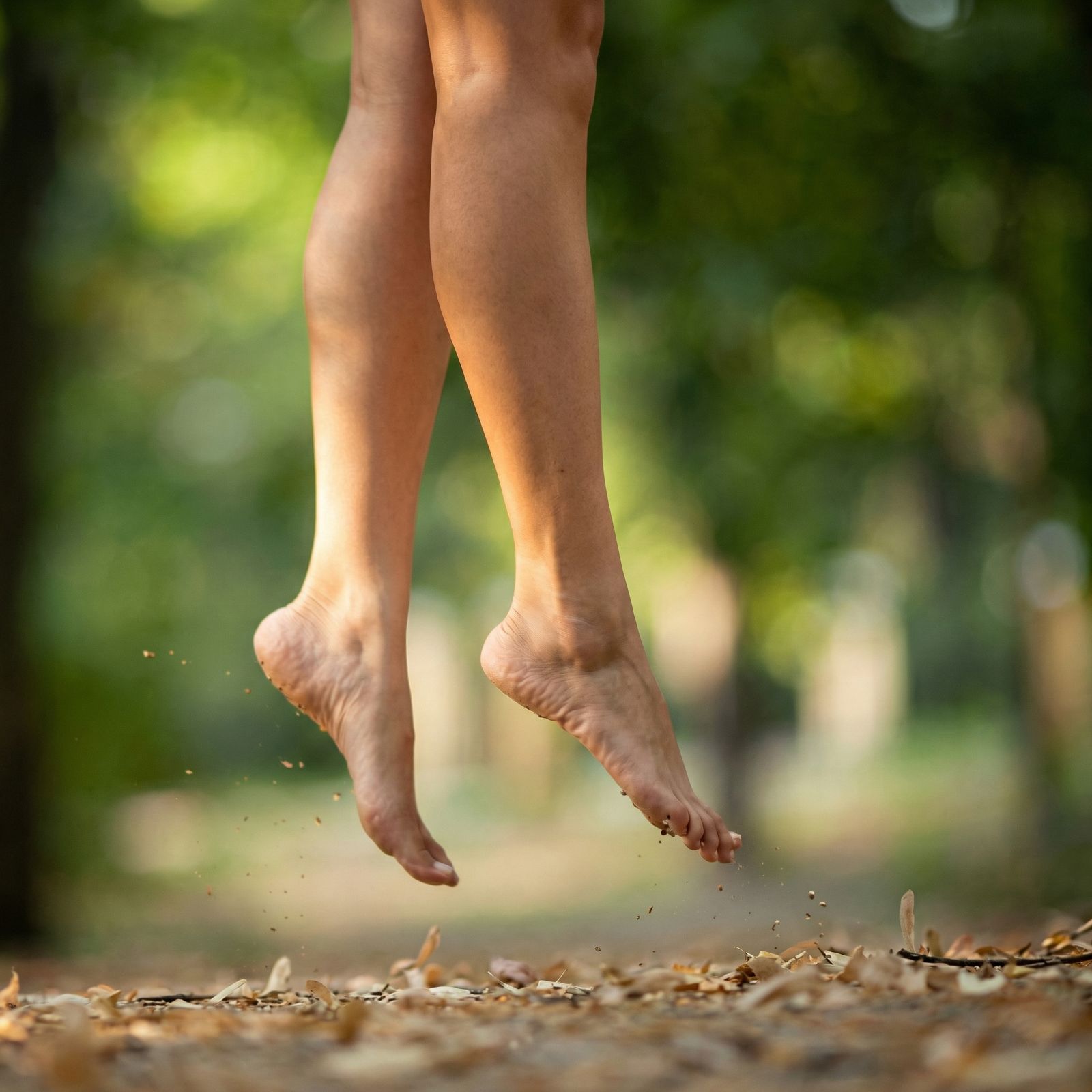 A person's bare feet and lower legs captured mid-jump over a leaf-covered forest floor.