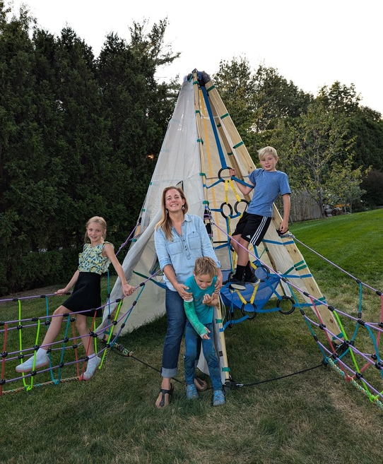 A family posing on a backyard climbing structure with trees in the background.