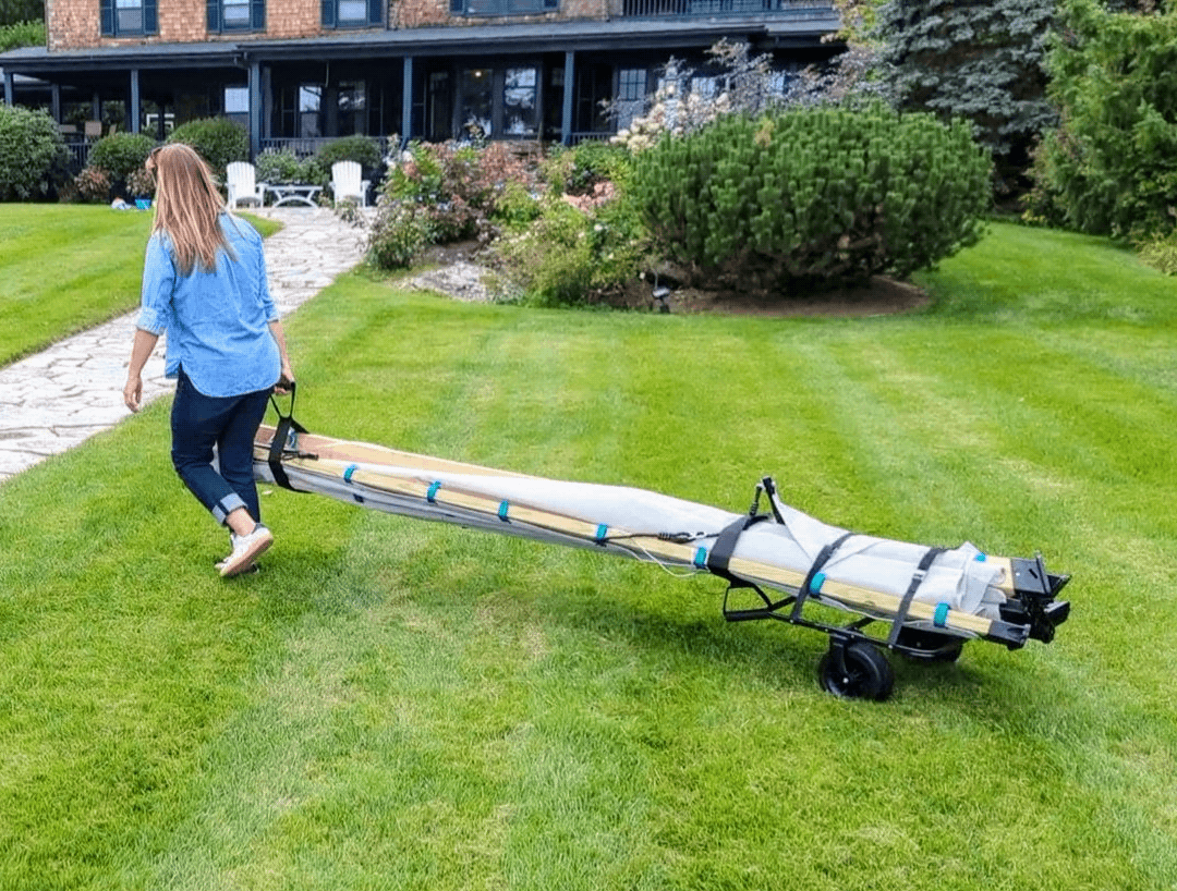 Person pulling a long cart on grass in front of a house.