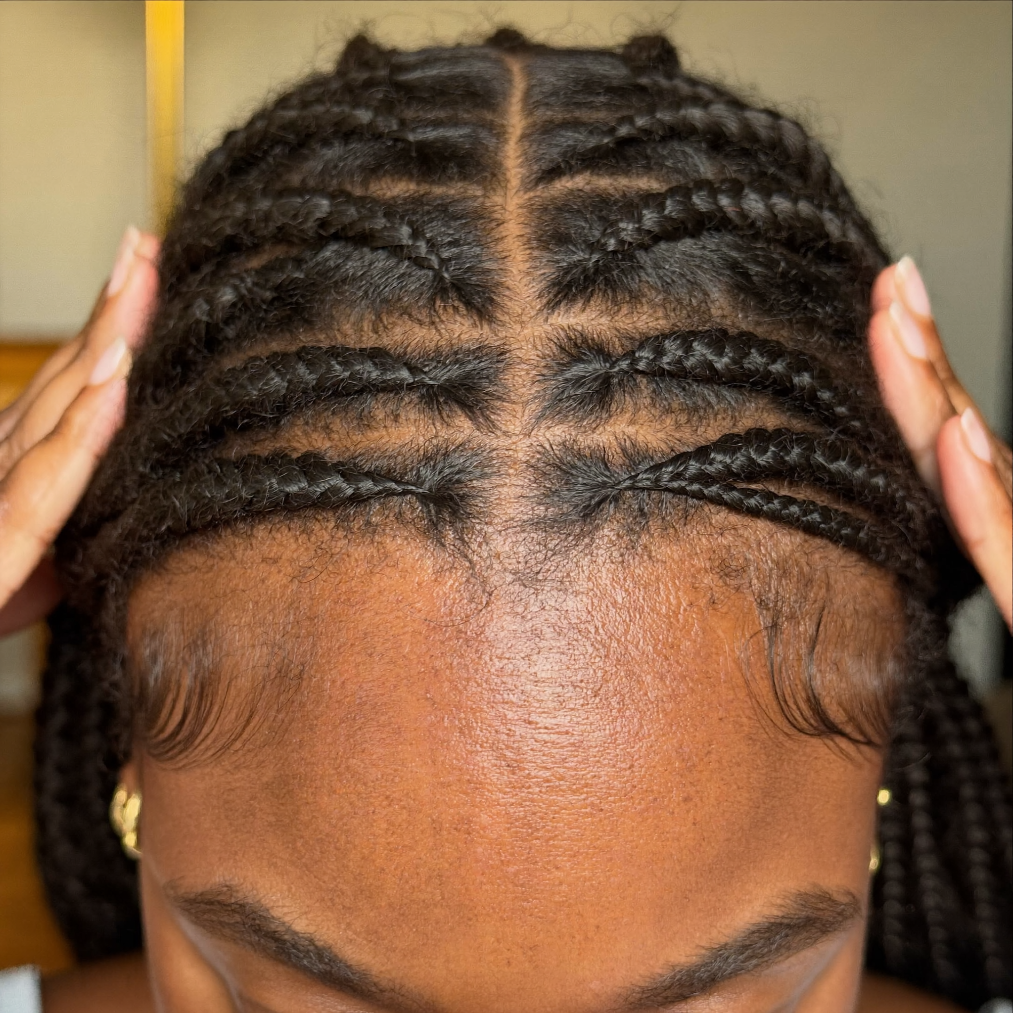 A close-up view of a person's scalp with neat, small braids parted down the middle.