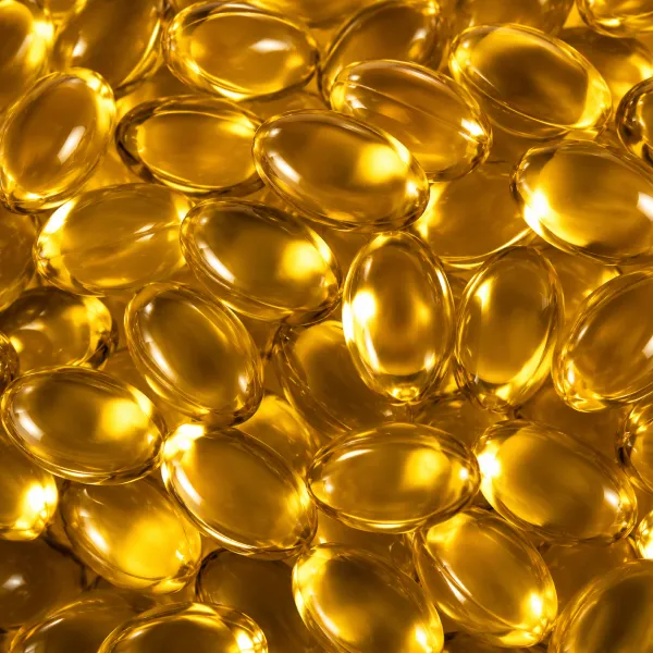 A close-up photograph of many shiny, golden-yellow softgel capsules piled together.