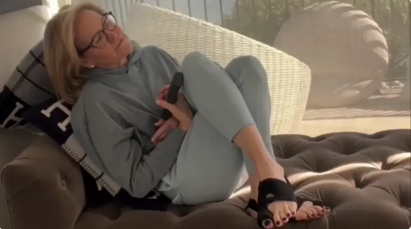 Person in casual clothes reclining on a couch, holding a phone.