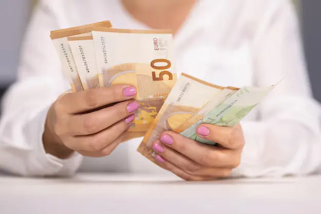 Person holding multiple euro banknotes with both hands on a table.