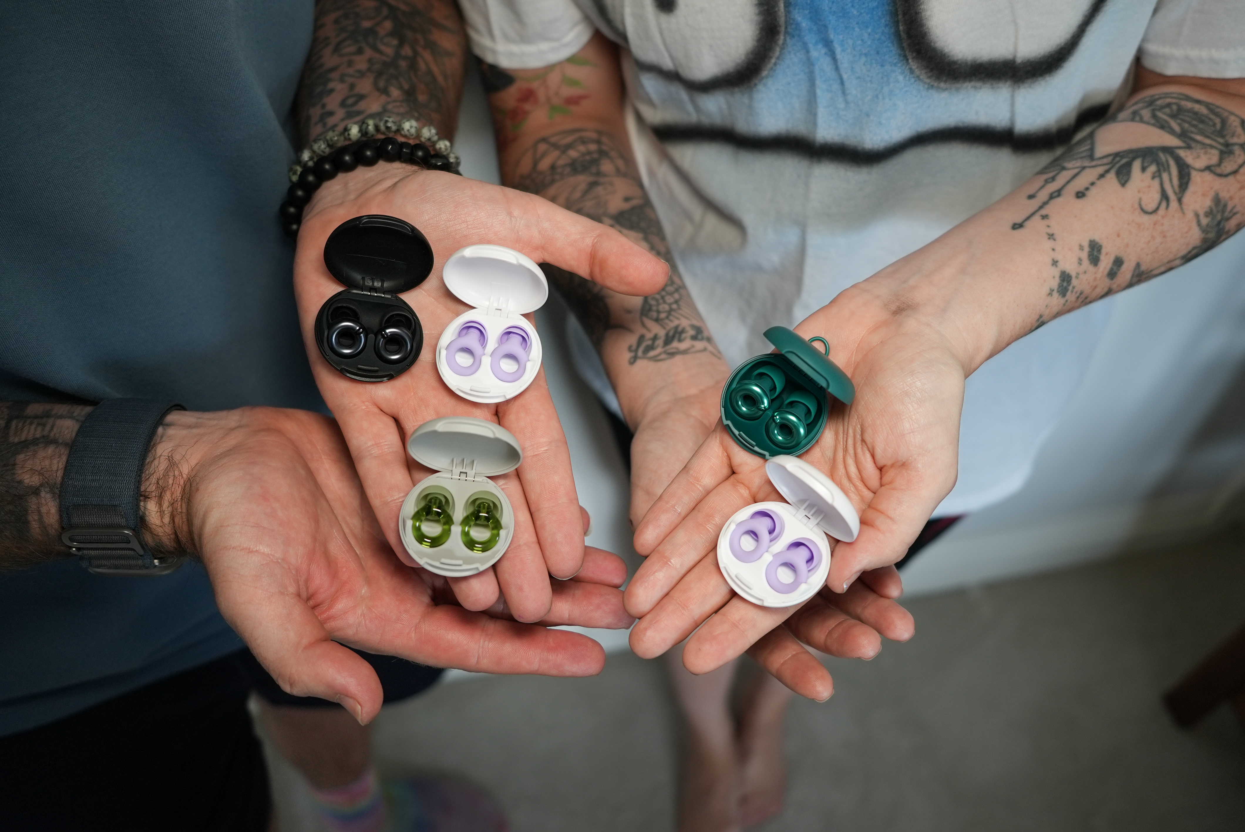 Two hands holding various colored earbud cases with earbuds inside.