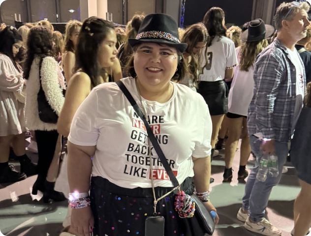 A person in a hat and themed shirt smiling in a crowded event setting.