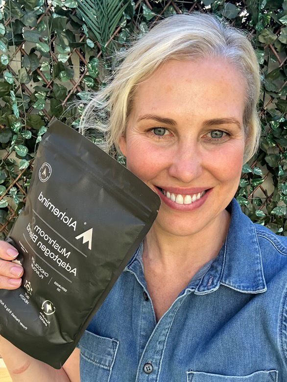 Person holding a black package labeled 'Mushroom Adaptogen Blend' in a garden setting.