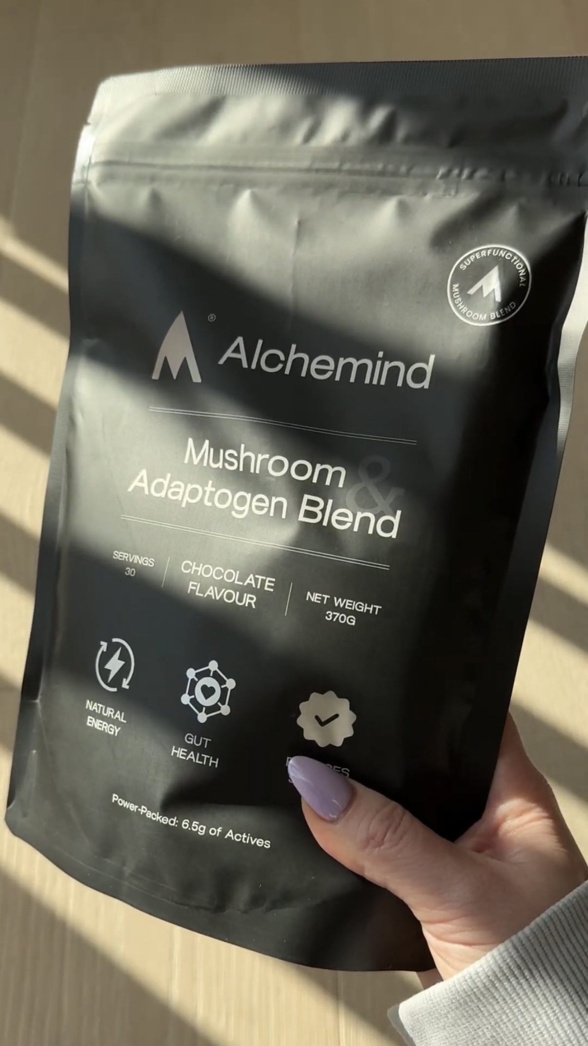 A hand holding a black Alchemind mushroom adaptogen blend package.
