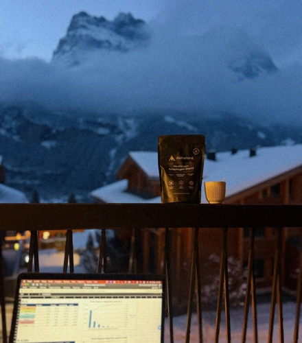 Laptop with charts, coffee, and mountain view from a balcony.