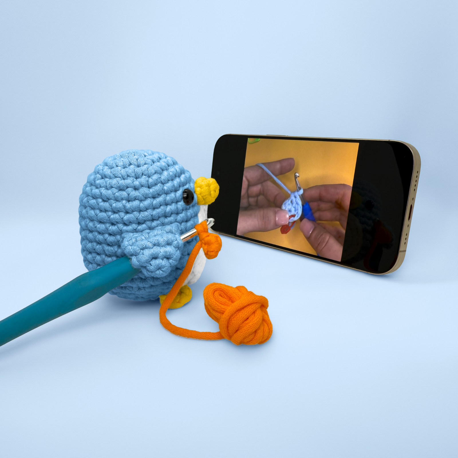 Crocheted penguin watching a crochet tutorial on a smartphone.