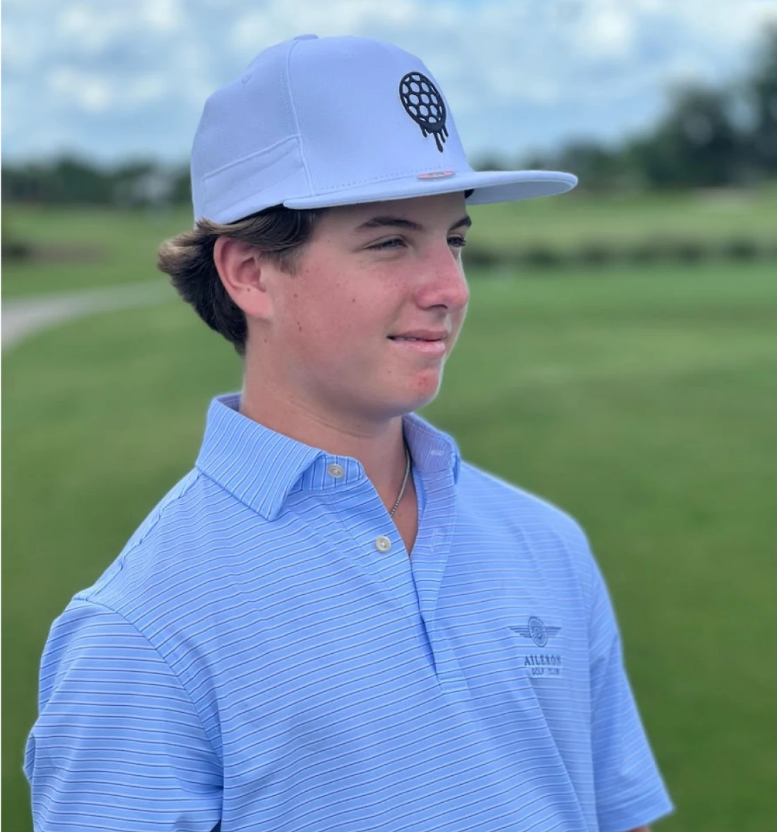 A young man in a blue striped polo shirt and a light blue cap on a golf course.