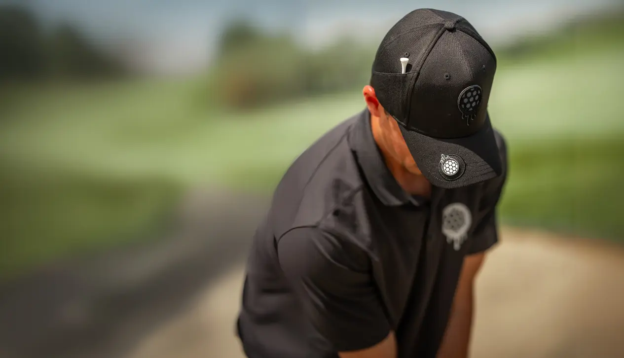Person in black cap and shirt, holding a golf club on a blurred background.