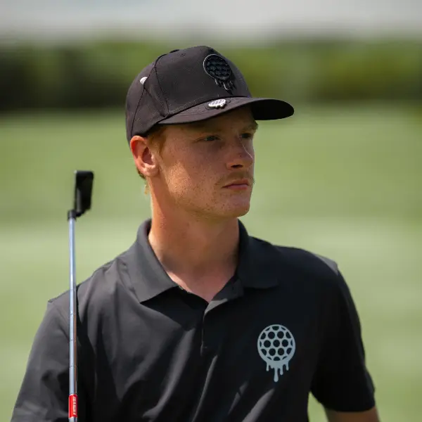 Person in a black cap and shirt holding a golf club on a golf course.