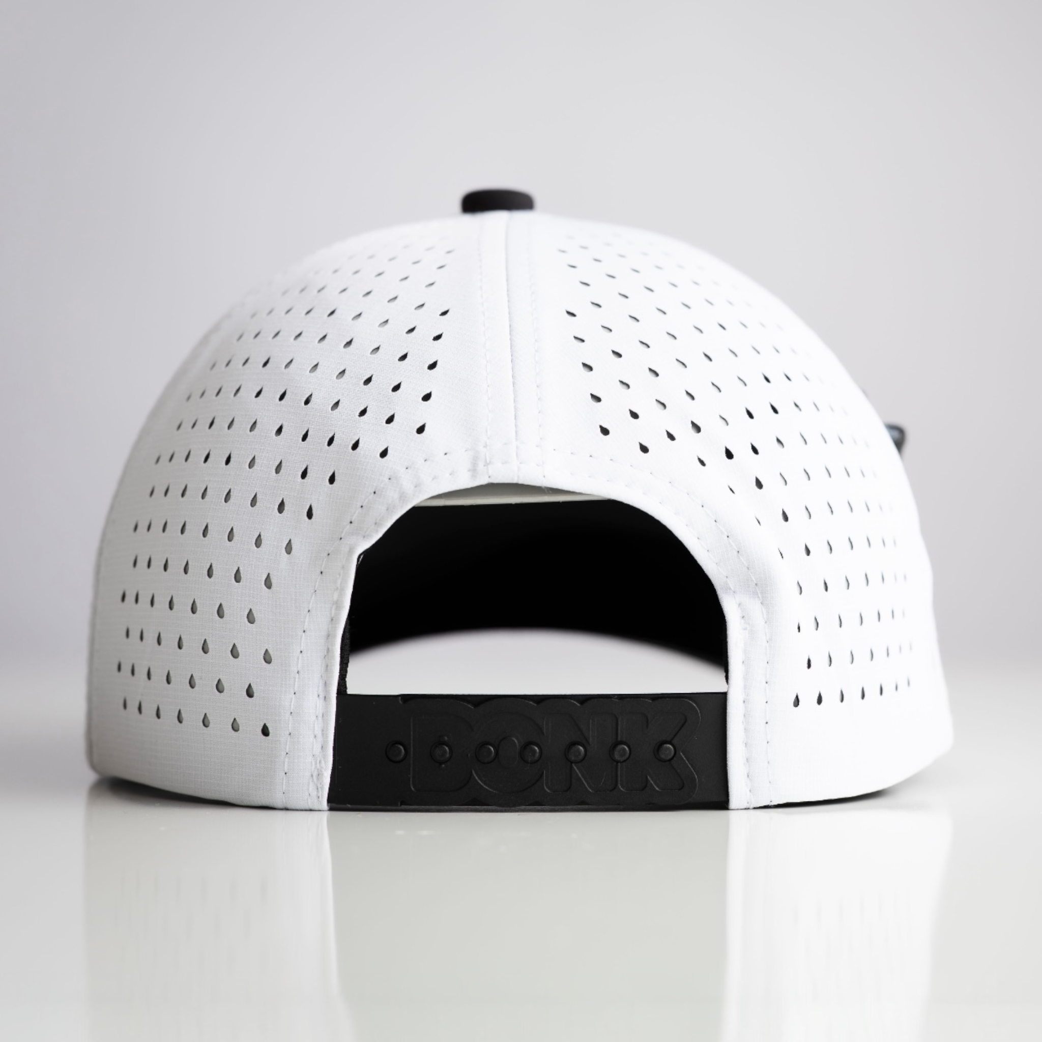 The back of a white perforated baseball cap with a black snapback closure embossed with the word DORK.