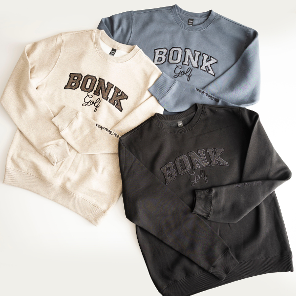 Three 'BONK Golf' crewneck sweatshirts in oatmeal, slate blue, and black, laid flat on a white surface.
