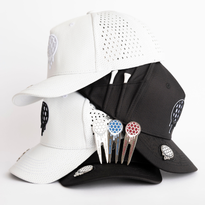 A stack of white and black perforated golf hats with matching divot tools and logo pins.