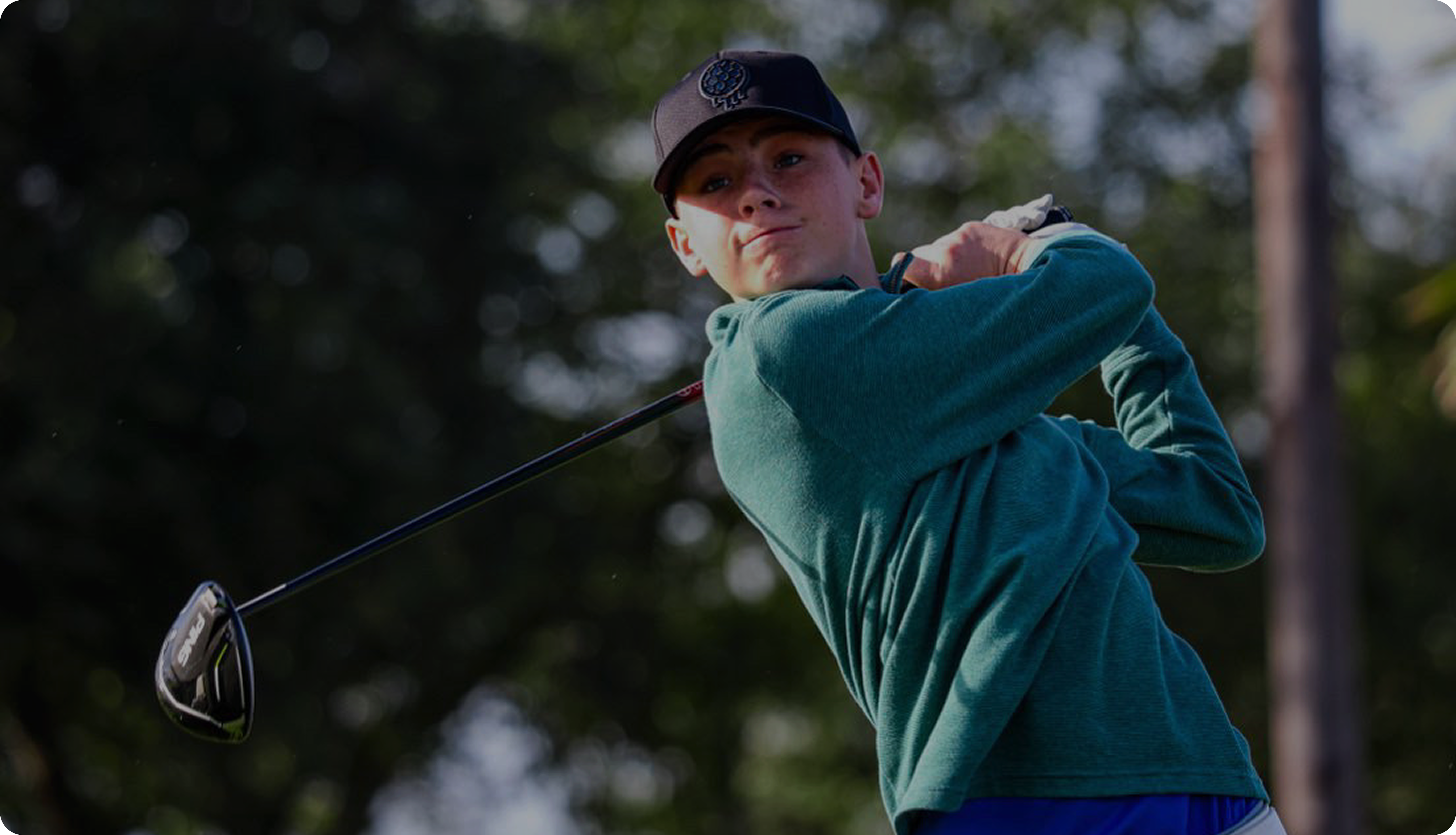 Person in a green shirt swinging a golf club outdoors.