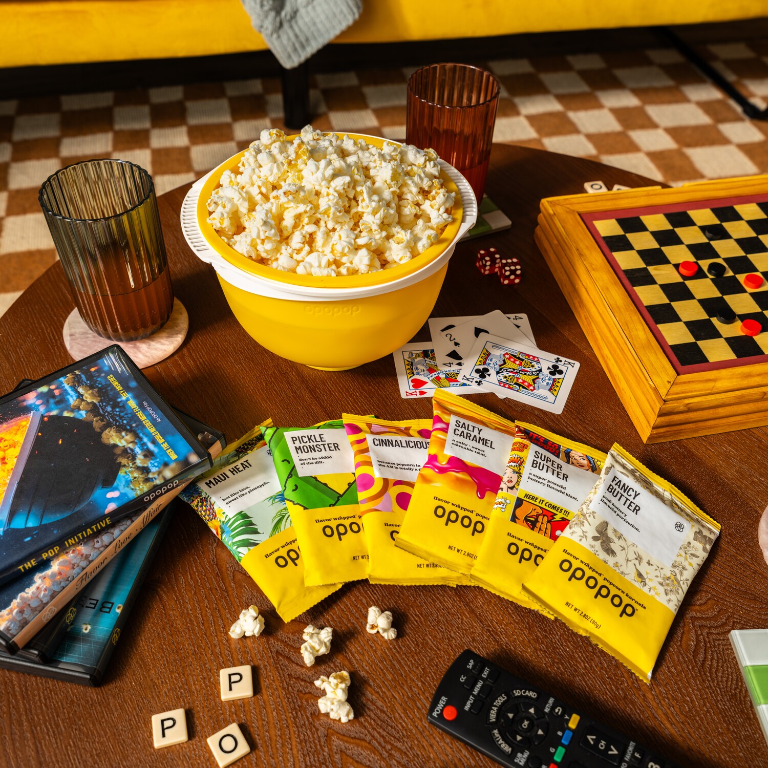 A coffee table with a bowl of popcorn, games, drinks, and various packets of flavored popcorn.