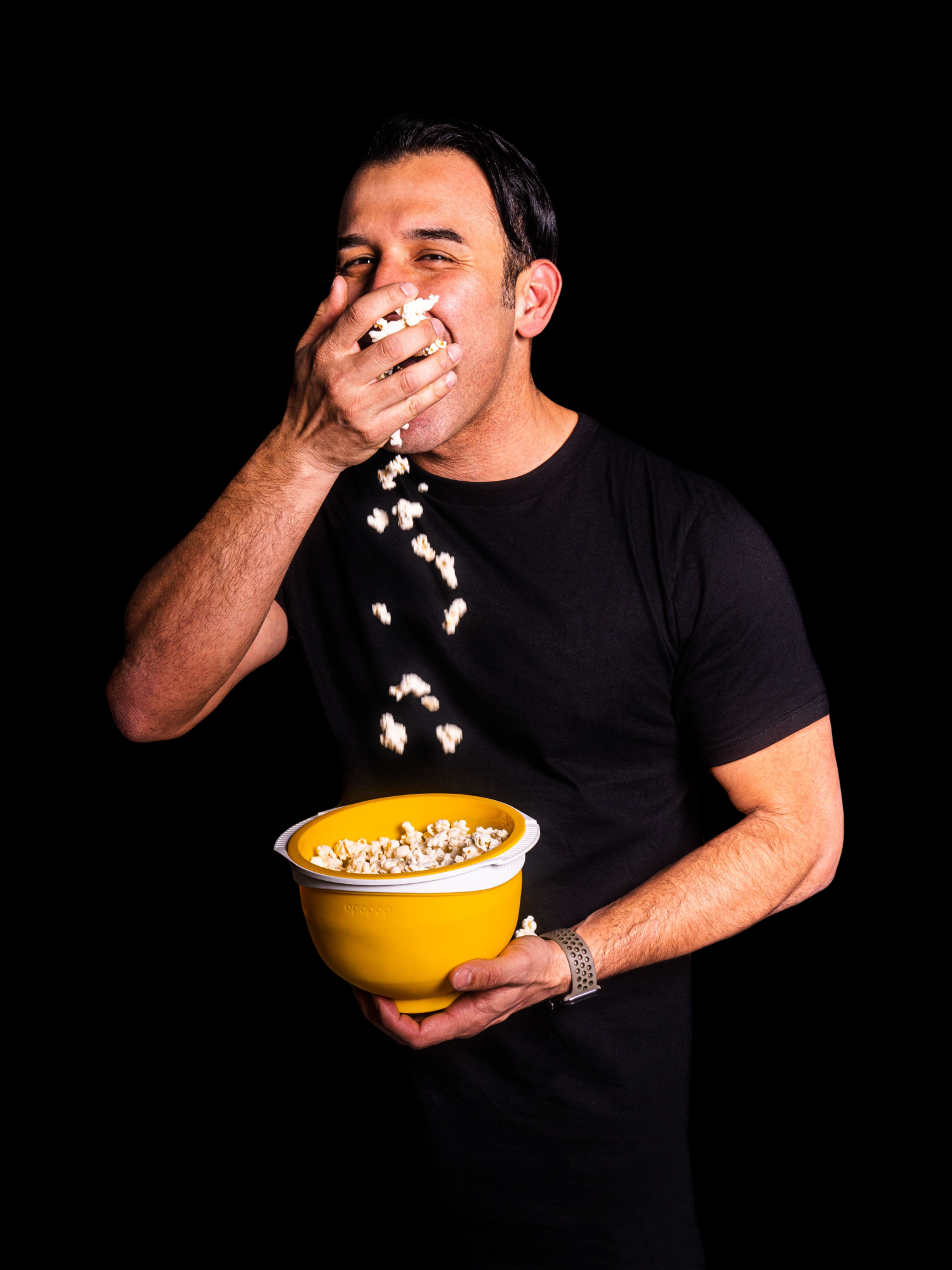 Person eating popcorn from a yellow bowl against a black background.