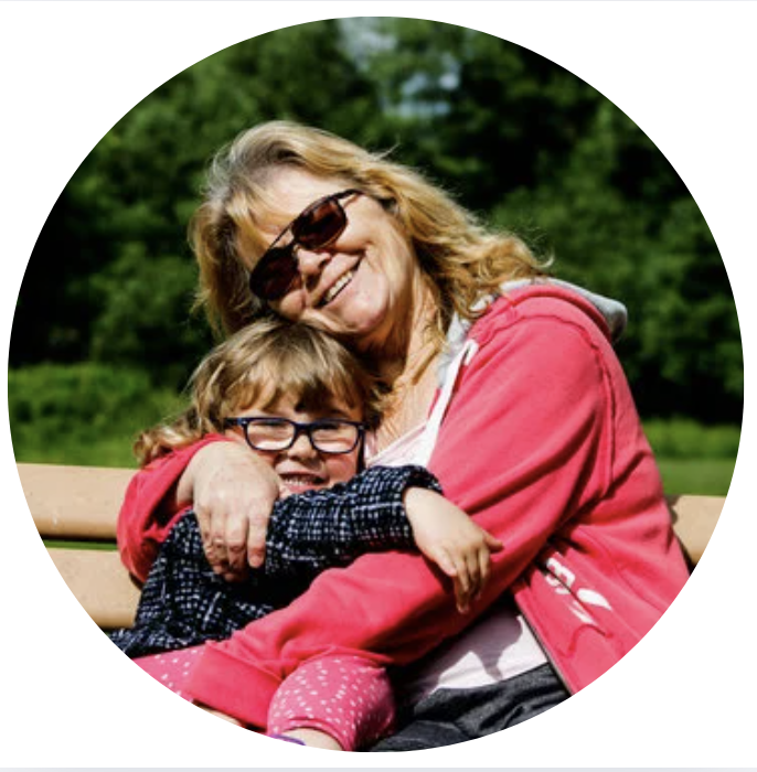 Woman and child with glasses hugging on a bench outdoors.