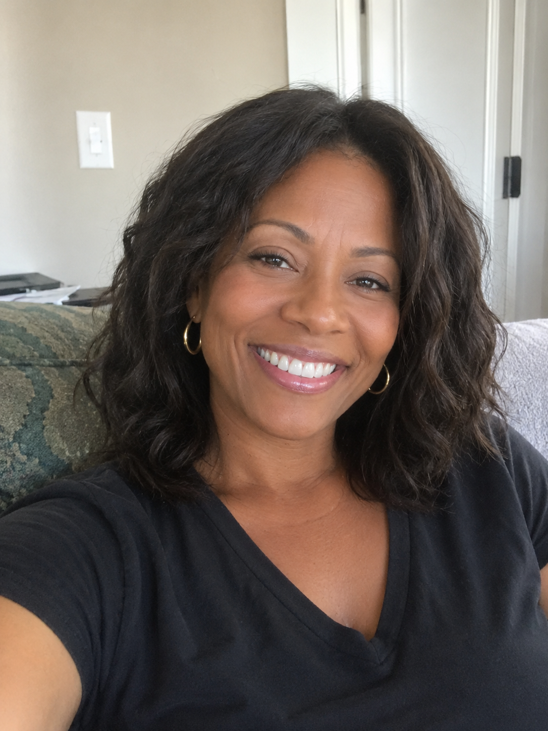 A smiling woman with dark wavy hair and a black t-shirt looks at the camera.