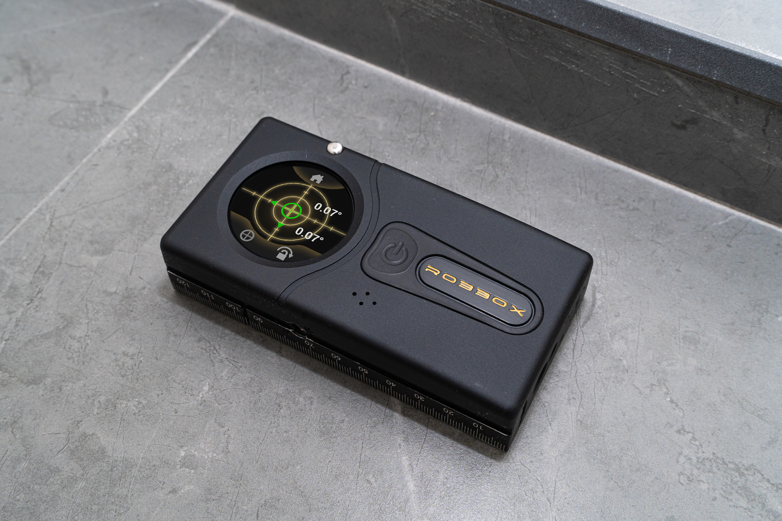 Black electronic device with digital display and power button on a gray surface.