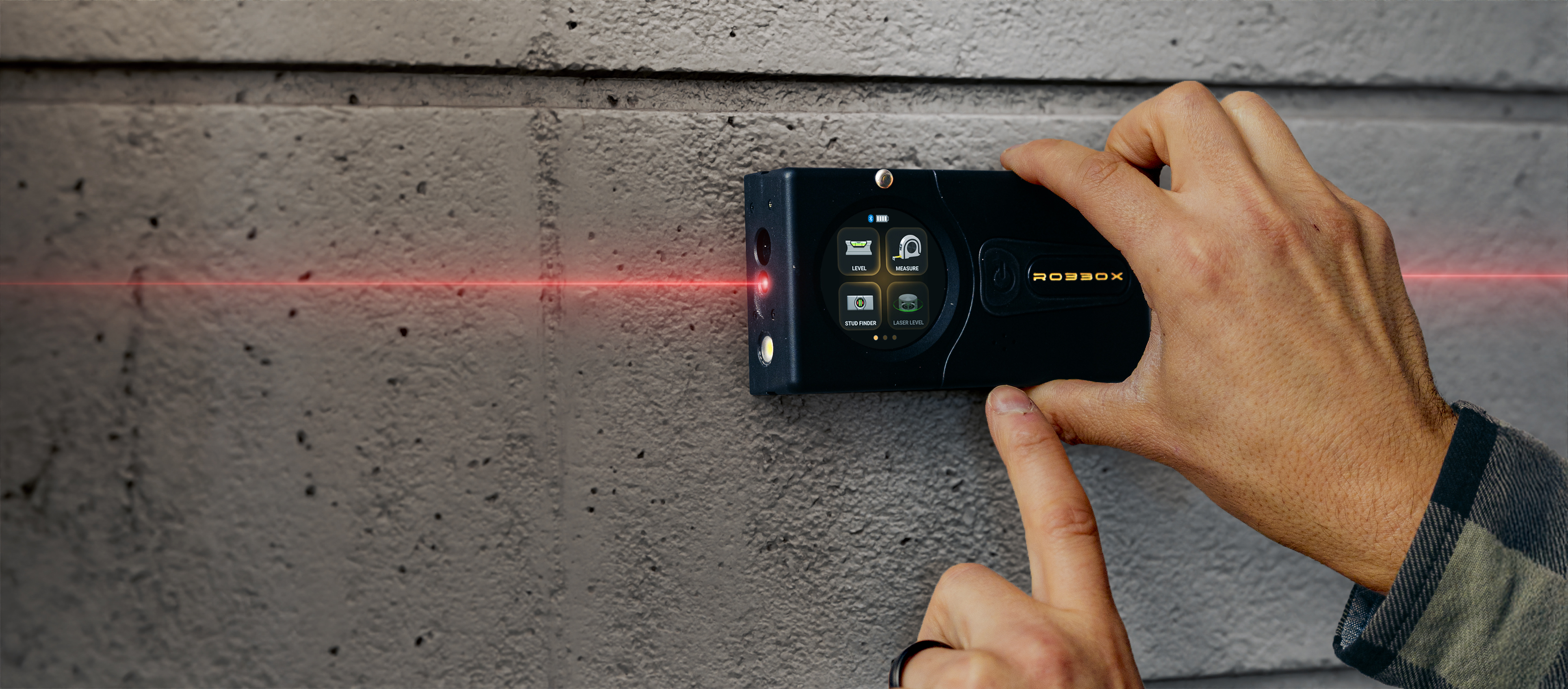 Hand operating a laser level tool against a textured wall.