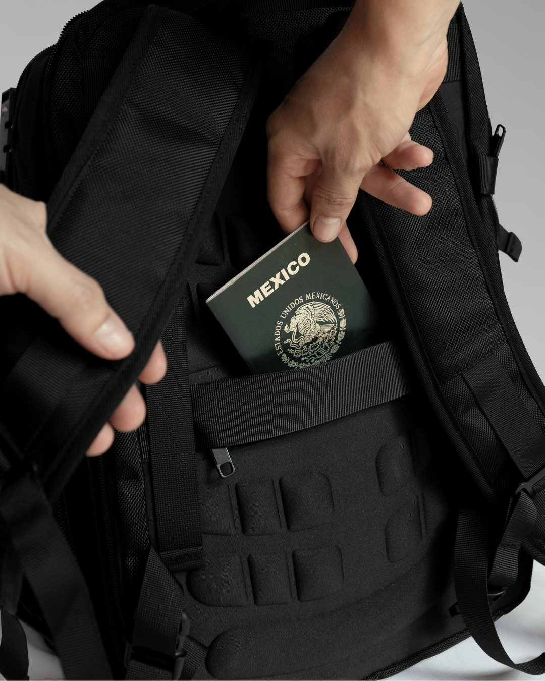 Hand placing a Mexican passport into a black backpack pocket.
