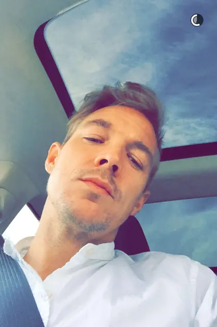 Person in a car with a sunroof, wearing a white shirt, looking at the camera.