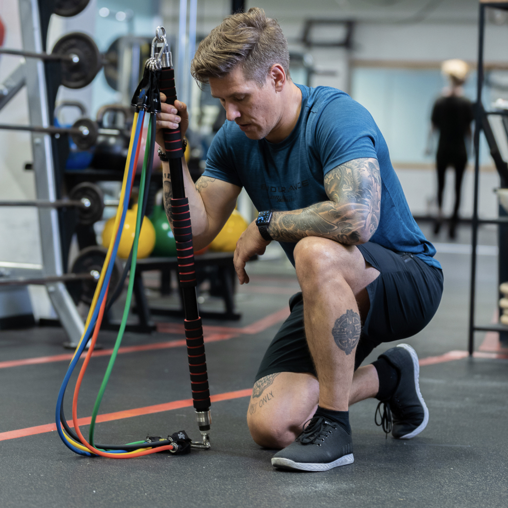 Man kneeling in gym holding exercise equipment with resistance bands.