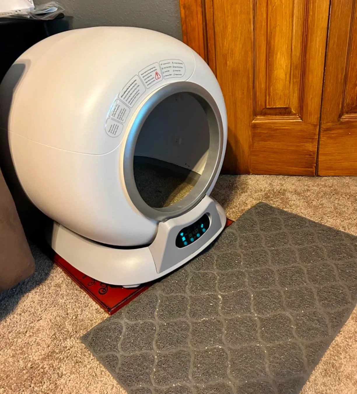 A white, automatic self-cleaning cat litter box sits on a carpet next to a grey litter mat.