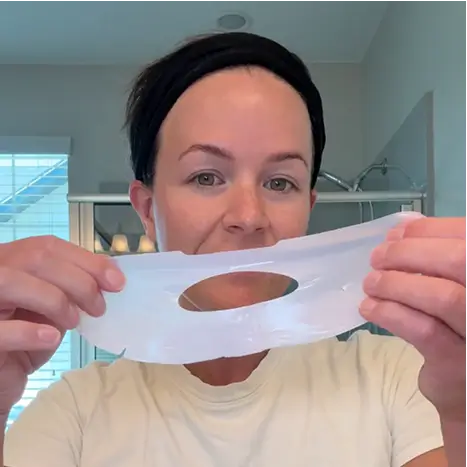 Person holding a white face mask in a bathroom.