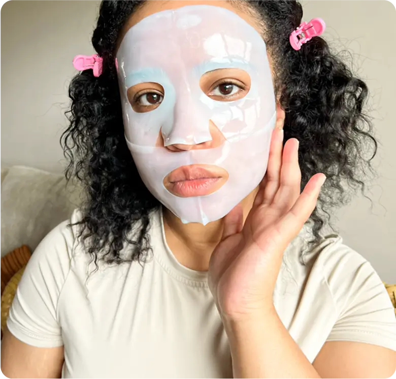 Person wearing a sheet mask with pink hair clips.
