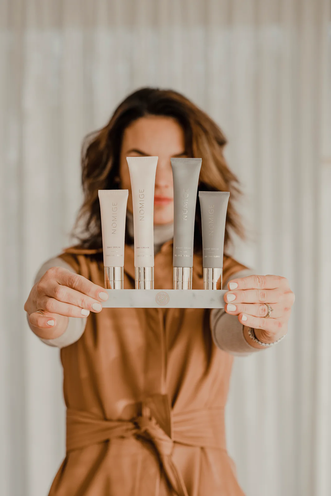 Person holding a set of four skincare product tubes against a blurred background.